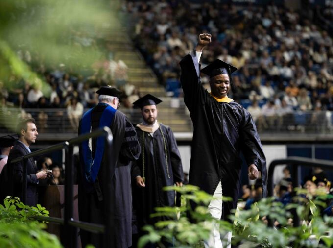 student crossing stage at commencement with hand raised in the air