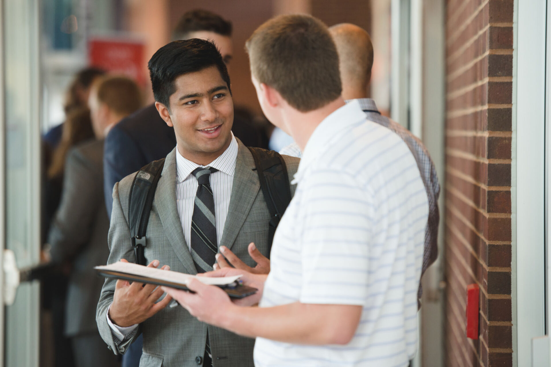 Professionally dressed person talks to another person with a portfolio and pen.