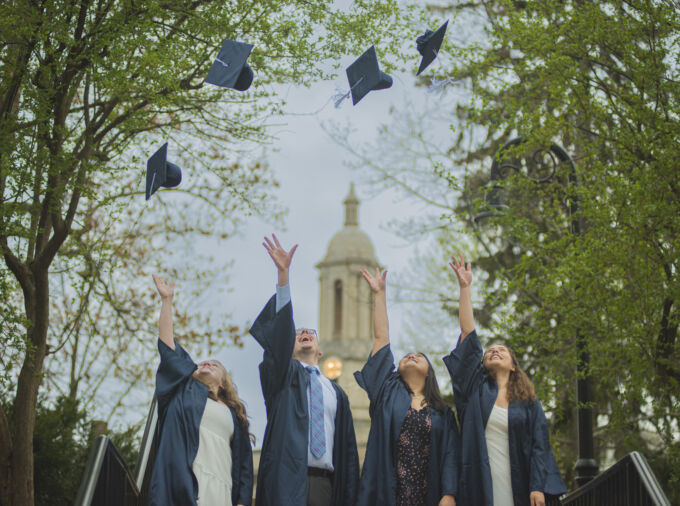 Recent graduates in robes tossing their hats into the air in front of Old Main.