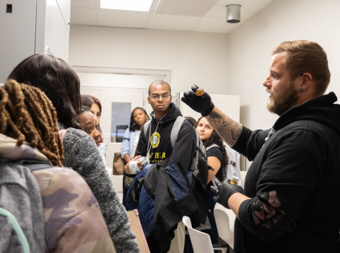 Students admiring a tour guide showing them a beaker with fluid in the lab